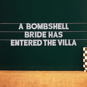 May include: A black chalkboard with white glitter letters spelling "A bombshell bride has entered the villa".