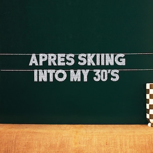 Op de afbeelding: Een zwart schoolbord met witte glitterletters die "Apres Skiing into my 30's" spellen.