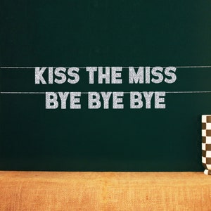 May include: A silver glitter banner with the text "Kiss the Miss Bye Bye Bye" hanging on a dark green chalkboard.
