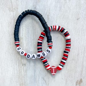 May include: Two beaded bracelets with black, white, and red beads. One bracelet spells out "GO DAWGS" and the other has a football charm.