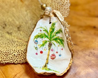 Op de afbeelding: Een handgeschilderd oester schelp ornament met een palmboom versierd met kleurrijke ornamenten. De oesterschelp is verguld en heeft een wit interieur.