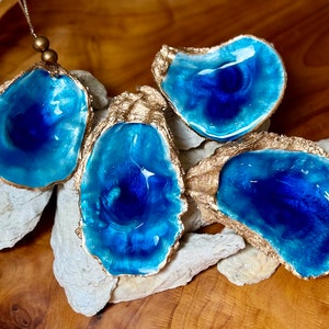 May include: Four blue and gold oyster shell dishes. The shells are filled with a deep blue resin and have a gold metallic finish.