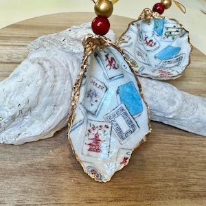 Op de afbeelding: Handbeschilderde oesterschelpversieringen met gouden rand, met speelkaartenmotieven. De schelpen zijn versierd met rode en gouden kralen om op te hangen. Deze ornamenten bieden een unieke, artistieke stijl, ideaal voor feestelijke decoratie of als een onderscheidend cadeau.