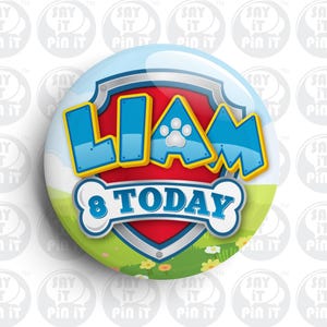Puede incluir: Una insignia redonda con un tema de la Patrulla Canina. La insignia es roja, azul y amarilla con una huella de pata blanca. El texto "Liam 8 Today" está en la insignia.