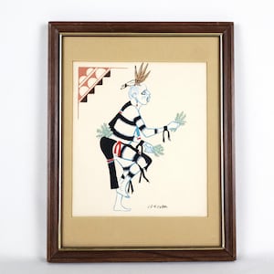 May include: A framed print of a Native American dancer in a black and white striped outfit, holding sprigs of green foliage. The dancer is painted in blue, red, and black against a cream background. The print is signed "J.D. Koyba."