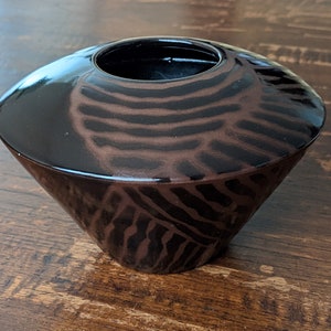 May include: A black and brown ceramic vase with a wide, shallow opening and a flared base. The vase has a unique, abstract pattern of stripes and swirls.