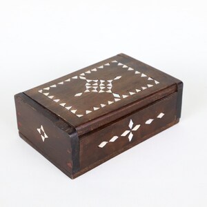 May include: A rectangular wooden box with a dark brown finish. The lid and sides are inlaid with white, geometric patterns. The box has a hinged lid and is likely used for storage or display.