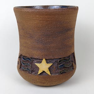 May include: A brown ceramic mug with a blue and gold design. The mug has a star and wavy lines around the middle.