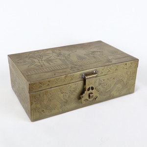 May include: A rectangular brass box with intricate engraved designs. The box features a hinged lid with a clasp closure. The sides and top are adorned with detailed illustrations of dragons, figures, and bamboo. The box is a vintage item.