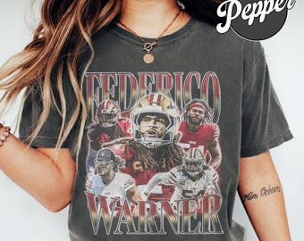 Puede incluir: Una camiseta gris carbón de manga corta con un estampado gráfico del jugador de fútbol americano Fred Warner en varias poses y uniformes. El texto "FEDERICO" aparece en la parte superior y "WARNER" en la inferior con una fuente roja y dorada.