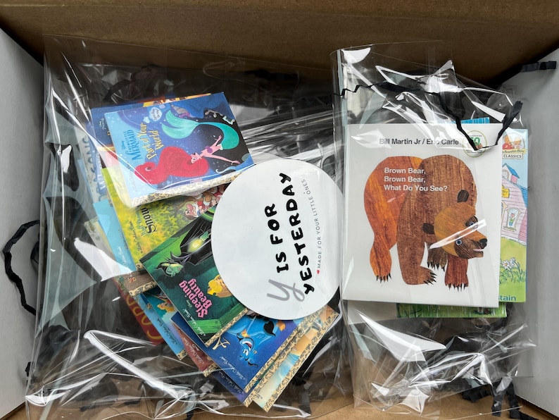 Pu&ograve; includere: Una collezione di libri per bambini confezionati in due sacchetti di plastica trasparente all'interno di una scatola di cartone. I libri includono titoli come Brown Bear, Brown Bear, What Do You See?, Sleeping Beauty e The Little Mermaid. Un adesivo circolare riporta la scritta Y IS FOR YESTERDAY.