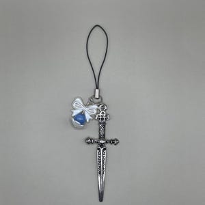 May include: A silver charm with a blue and white bow and a silver dagger charm attached to a black string.