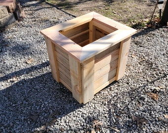 May include: A square wooden planter box made from natural wood planks. The planter has a simple design with a raised lip around the top.