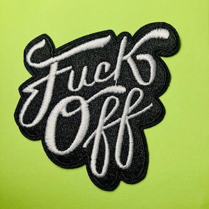 May include: A black embroidered patch featuring the white text "Fuck Off" in a cursive script font. The patch has a thick black border that follows the contour of the lettering, creating a bold contrast between the white thread and black background.
