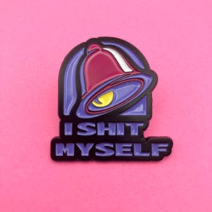 Peut inclure: Une broche en émail métallique représentant un graphique de cloche stylisé dans des tons de violet, rouge et jaune. Sous la cloche, le texte I SHIT MYSELF est gravé en lettres capitales violettes sur un fond noir, créant un design graphique.