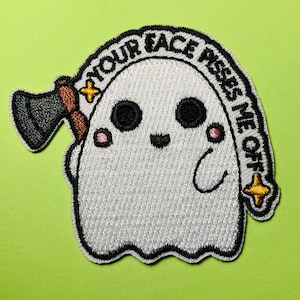 May include: An embroidered patch featuring a white ghost with black eyes and pink cheeks, holding a dark gray axe with a brown handle. The text "YOUR FACE PISSES ME OFF" is arched above the ghost, accented by two small yellow four-pointed stars.