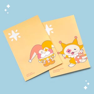 Peut inclure: Deux cahiers jaunes avec des illustrations de clowns de dessins animés. Un clown porte un chapeau rose et orange, l'autre un chapeau jaune avec des accents roses. Le texte sur les cahiers se lit "reach your full potential" et "everything will be honky dory."