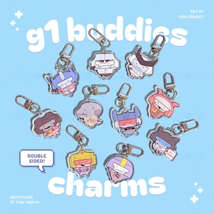 May include: A collection of cartoon character charms with keychains. The charms are double-sided and feature various characters in different colors. The background is light blue with the text "g1 buddies" and "charms". The text "DOUBLE SIDED!" is also visible.