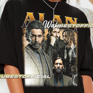 Pode incluir: Camiseta preta com um gráfico de um homem e o texto dourado "ALAN". A imagem inclui o texto "Wave" e "UBESTOFFICIAL". O design é em estilo vintage.