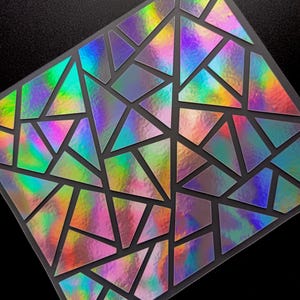 Puede incluir: Una lámina de pegatinas iridiscentes con un diseño geométrico. Las pegatinas están cortadas en varias formas triangulares y cuadriláteras, creando un patrón similar a un mosaico. Los colores cambian de verde a morado y rosa.