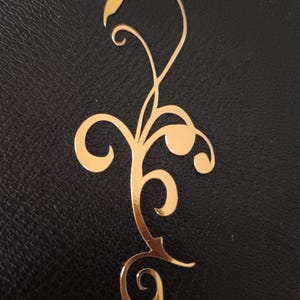 May include: A gold-colored metal bookmark with a decorative floral design.