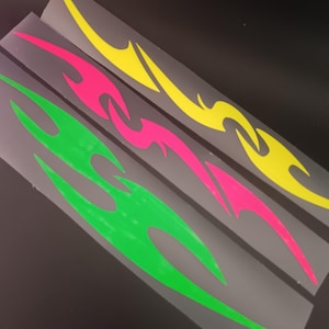 Op de afbeelding: Drie zelfklevende stickers met langwerpige, vlamachtige tribale patronen in felle neonkleuren. De bovenste sticker is felgeel, de middelste is felroze en de onderste is limoengroen. Elk ontwerp is gedrukt op een doorzichtige, rechthoekige ondergrond.