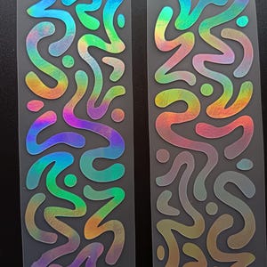 May include: Two sheets of iridescent stickers with abstract, wavy designs. The stickers have a rainbow color gradient, shifting from blues and greens to yellows and oranges. The designs are on a clear backing.