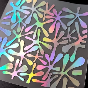 Peut inclure: Une feuille d'autocollants irisés en forme d'éclaboussures. Les autocollants ont un effet holographique, affichant une gamme de couleurs comprenant le rose, le vert, le bleu et le jaune. Les formes varient en taille et sont disposées sur un support transparent rectangulaire.