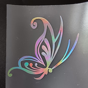 May include: A holographic butterfly sticker with a rainbow iridescent finish. The butterfly design features detailed wing patterns and curved antennae. The sticker is on a transparent backing, ready for application. Suitable for crafts and decorations.