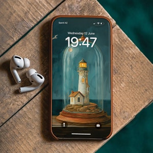 Puede incluir: Un teléfono inteligente con una funda de cuero marrón que muestra un faro bajo una cúpula de vidrio. La hora es 19:47 y la fecha es miércoles 12 de junio. El teléfono está sobre una superficie de madera con dos auriculares inalámbricos blancos.