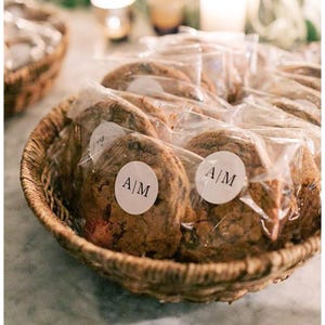 May include: A wicker basket containing individually wrapped cookies. Each cookie is sealed in clear plastic and has a white circular sticker with the letters "A|M". The cookies are a light brown colour.