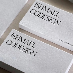 May include: Close-up of white business cards with the name "ISHMAEL CODESIGN" embossed in black. The website address www.website.com is printed in a smaller font. The cards have a textured surface.