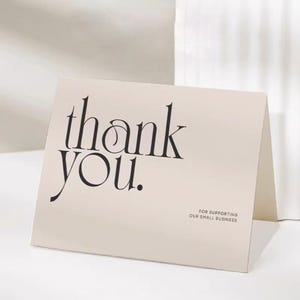 Peut inclure: Une carte pliée beige avec les mots "thank you" en écriture noire élégante. La carte comprend également le texte "FOR SUPPORTING OUR SMALL BUSINESS" en plus petit.