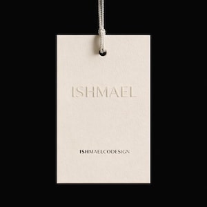 Peut inclure: Étiquette rectangulaire crème avec le mot "ISHMAEL" en relief et le texte "ISHMAELCODESIGN". Une ficelle blanche est attachée en haut, le tout sur un fond noir.