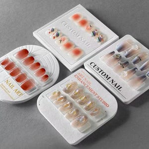 May include: A selection of custom nail sets in diverse designs and colours. The sets feature ombre, glitter, and patterned nails, presented in white packaging with the text "CUSTOM NAIL" and "NAIL ART".