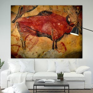 May include: A red and black cave painting of a bison on a yellow and brown background. The painting is on a wall and is a classic example of prehistoric art.