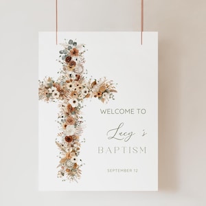 May include: A vertical rectangular sign featuring a large cross composed of dried flowers and foliage in shades of cream, beige, and rust orange. The text reads: WELCOME TO, Lucy's, BAPTISM, SEPTEMBER 12, printed in a dark gray sans-serif font.