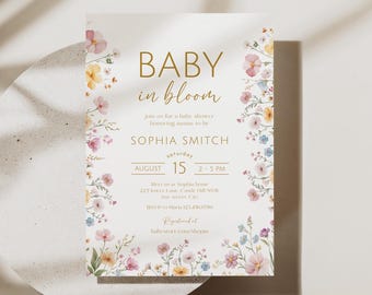 May include: Baby shower invitation with floral accents. The invitation features the words "BABY in bloom" in gold script. The invitation includes the date, time, and location of the baby shower, along with the name of the mother-to-be, Sophia Smitch.