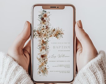 May include: A smartphone displays a baptism invitation. The invitation features a floral cross design in neutral tones. Text includes "Baptism of our daughter," date, time, church address, and RSVP information. The phone is held by a person wearing a cream-colored sweater.