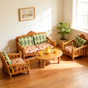 May include: A miniature wooden living room set comprising a two-seater sofa, two armchairs, and a coffee table. The sofa and armchairs feature floral cushions and green diamond-patterned back cushions. A yellow teapot and cups are on the table. A framed picture hangs on the wall.