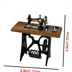 K&ouml;nnte beinhalten: Eine Miniatur-N&auml;hmaschine mit einem Holztisch und einem schwarzen Metallsockel. Die Maschine hat goldfarbene Akzente und einen roten Knopf. Der Tisch ist 7,11 cm breit und 7,37 cm hoch.