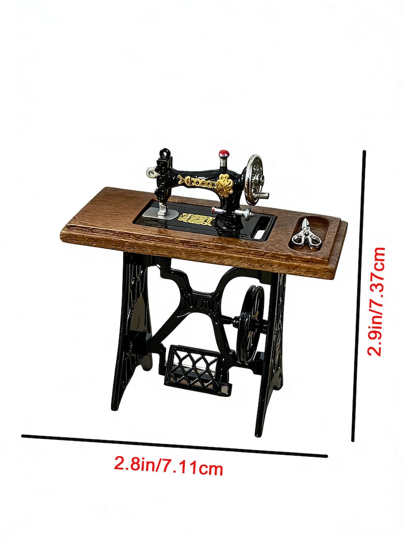 K&ouml;nnte beinhalten: Eine Miniatur-N&auml;hmaschine mit einem Holztisch und einem schwarzen Metallsockel. Die Maschine hat goldfarbene Akzente und einen roten Knopf. Der Tisch ist 7,11 cm breit und 7,37 cm hoch.