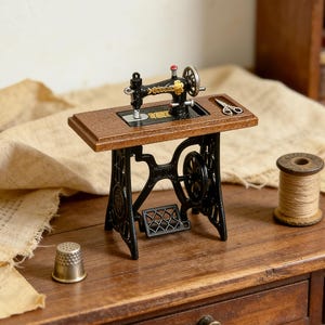 K&ouml;nnte beinhalten: Eine Miniatur-Antik-N&auml;hmaschine mit einem schwarzen Gusseisenfu&szlig; und einer Holzplatte. Die Maschine hat goldene Akzente und einen roten Knopf. Ein Fingerhut, eine Schere und eine Garnrolle sind ebenfalls vorhanden.