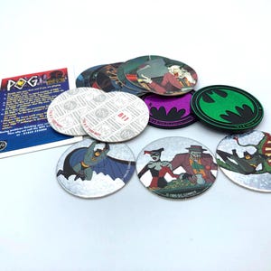 May include: A collection of Batman POGs featuring various characters like Batman, Harley Quinn, and the Joker. The POGs have colorful designs and are made of a metallic material. A POG card is also included.