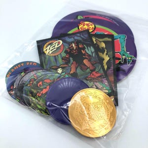 Puede incluir: Una colección de pogs y cromos de Planet Zed en una bolsa de plástico transparente. Los pogs son circulares con varios diseños de personajes. Las tarjetas comerciales presentan ilustraciones de criaturas fantásticas. También se incluye una moneda dorada.