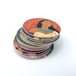 Könnte beinhalten: Ein Stapel runder, bunter, bedruckter Papieruntersetzer mit verschiedenen Disney-Charakteren. Der oberste Untersetzer zeigt Pocahontas, eine indianische Prinzessin, vor einem roten, goldenen und grünen Hintergrund.