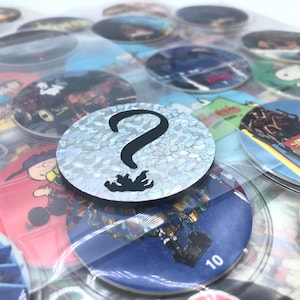 May include: A collection of circular collectible items, some with images and others with numbers. One item features a silver holographic background with a black question mark. The items are stored in a clear plastic sheet.