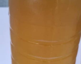 May include: A clear plastic bottle filled with a light amber liquid. The bottle has a rounded shape with horizontal ridges. The liquid appears to be a beverage or a solution.