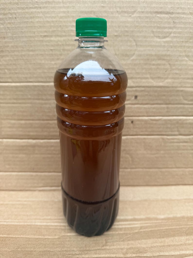 May include: A clear plastic bottle filled with a dark amber liquid, featuring a ribbed cylindrical body and a solid green screw-top cap. The container is transparent, allowing the deep brown color of the liquid inside to be clearly visible.