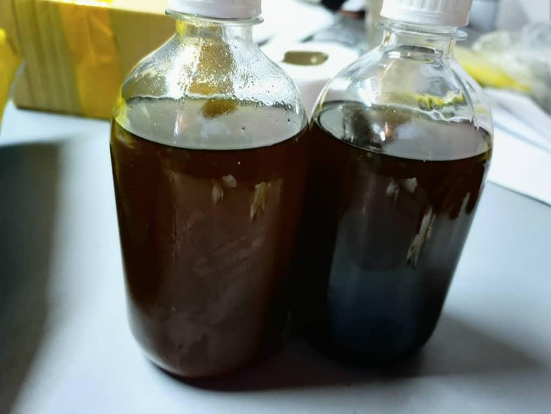 May include: Two clear glass bottles with white screw-top caps, each filled with a dark brown liquid. The bottles have a rounded shoulder and a cylindrical body, containing a translucent, amber-toned fluid that appears consistent in both containers.